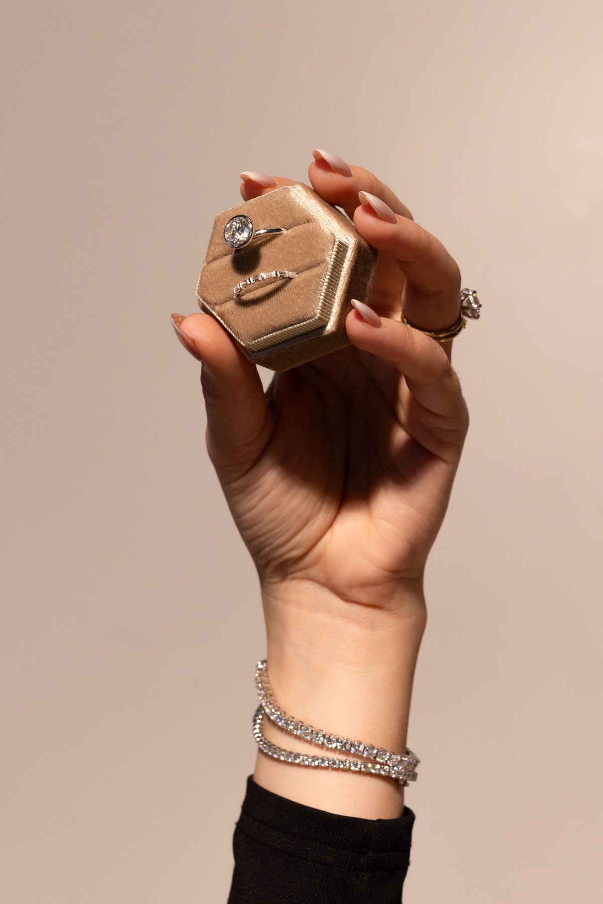 Hand holding a velvet ring box featuring a sparkling moissanite engagement ring and matching band.