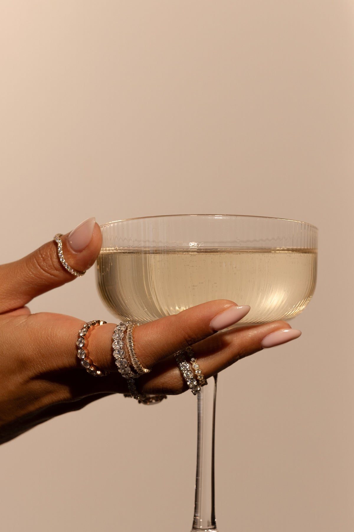Hand holding a champagne glass adorned with stacked TOVAA moissanite wedding bands in gold and silver.