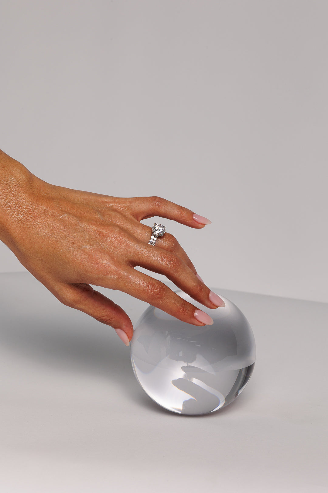 Hand with round moissanite engagement ring resting on sphere