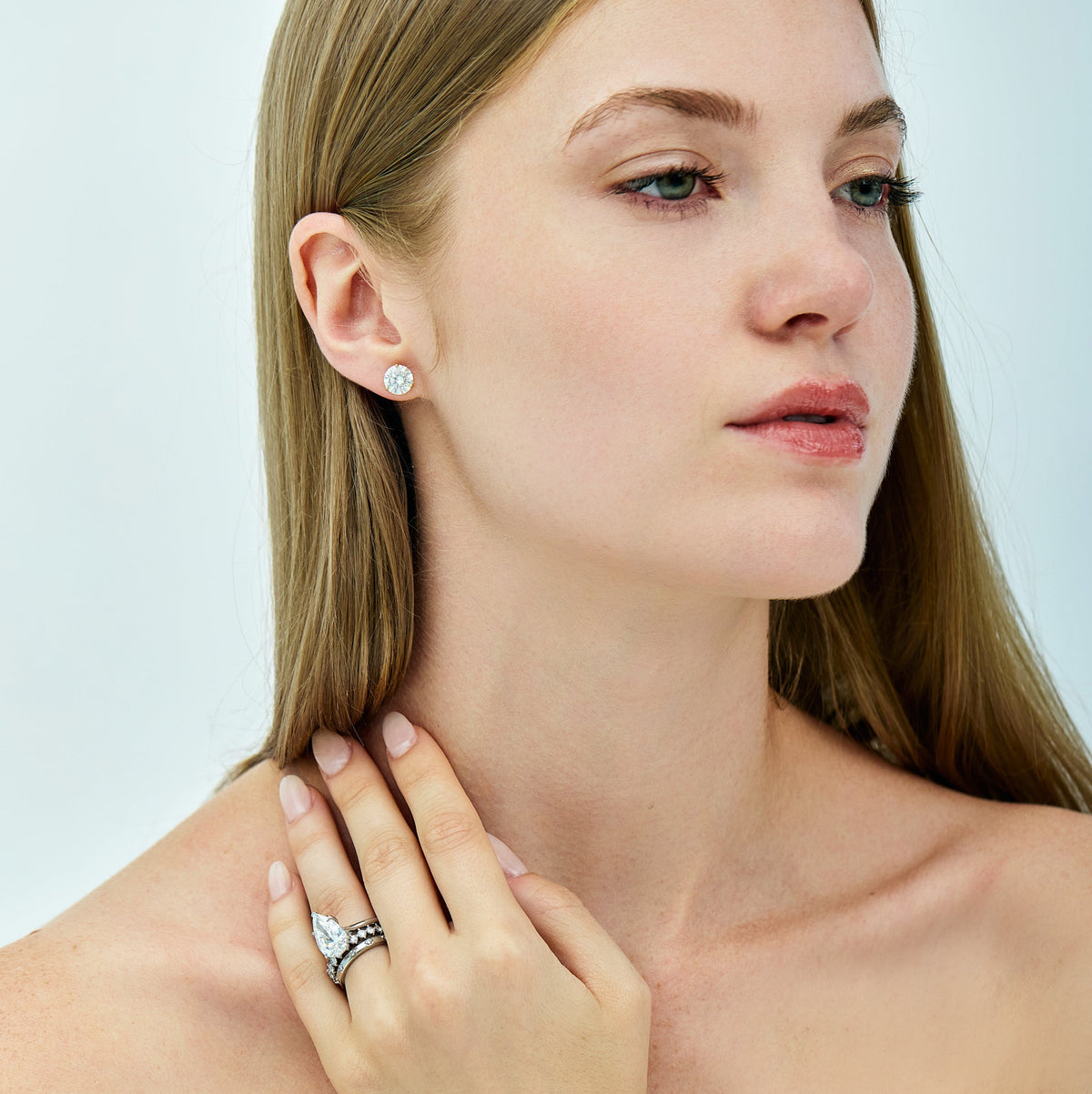 A woman wearing a silver-toned ring with a large clear center stone and smaller side stones, shown in a close-up portrait. She is also wearing a matching small stud earring.