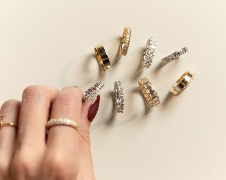 Moissanite engagement rings in yellow and white gold arranged in a circular layout, featuring oval, emerald, and round center stones with varied band styles.