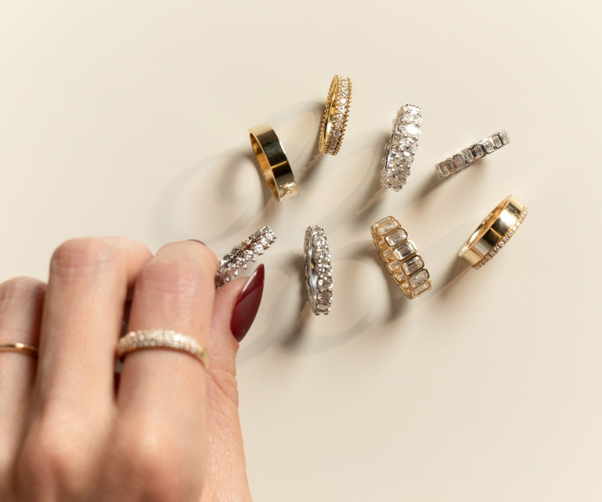 Hand holding a champagne glass adorned with stacked TOVAA moissanite wedding bands in gold and silver.