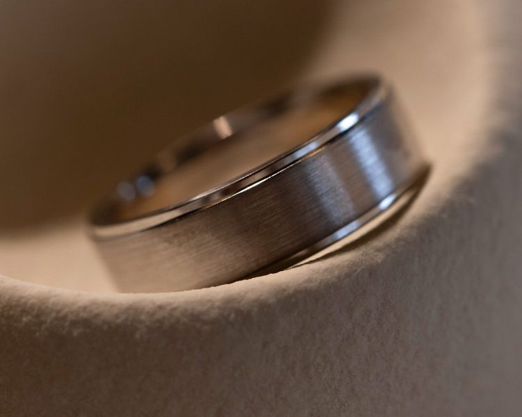 Close-up of a brushed metal men’s wedding band with polished edges, set into a curved stone form.