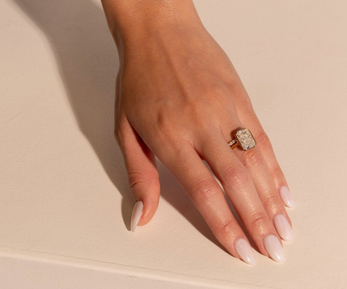 Hand model wearing a solitaire TOVAA radiant cut engagement ring in yellow gold with neutral manicure styling.