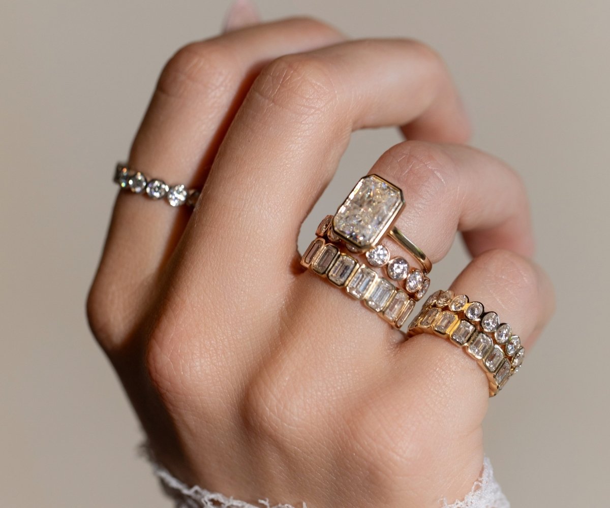 Woman wearing stacked TOVAA radiant cut engagement rings with baguette and round diamond bands in yellow gold.