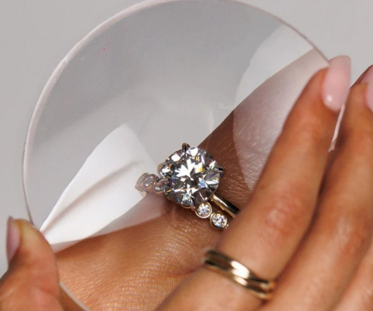 Hand with round moissanite engagement ring resting on sphere