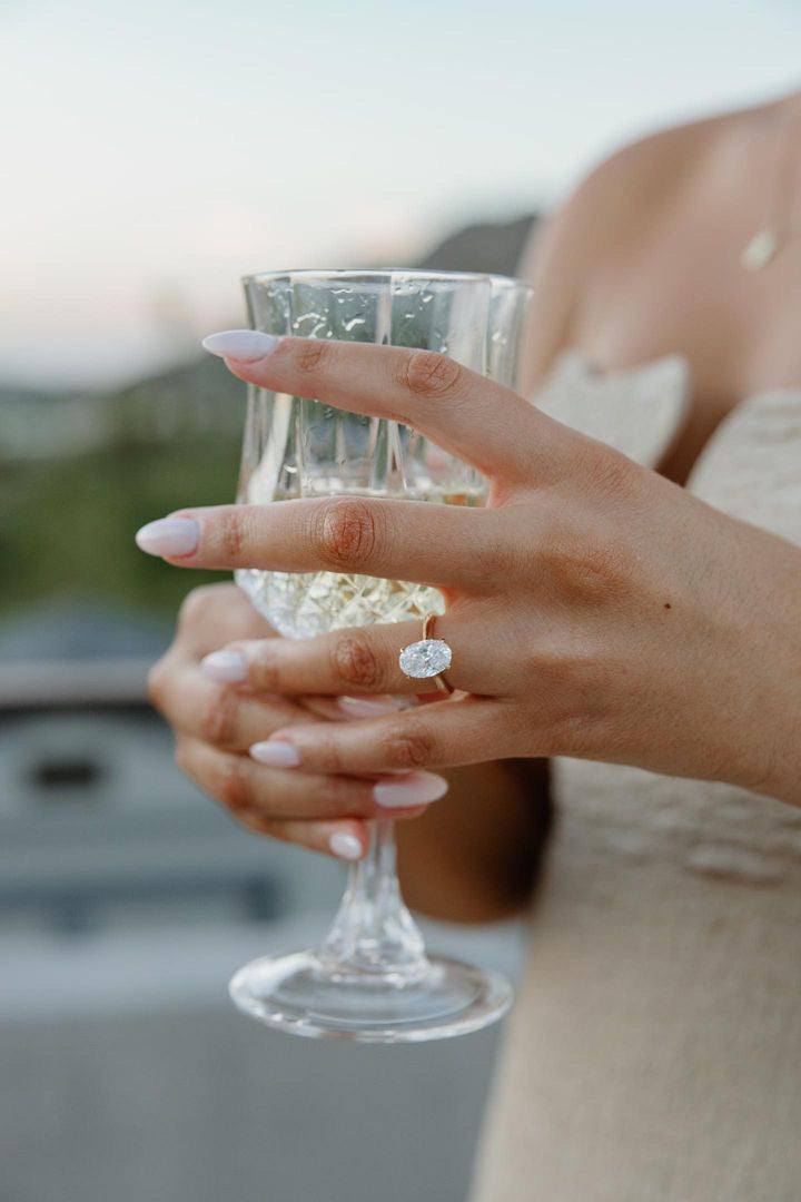 Woman holding a champagne glass while wearing a sparkling TOVAA lab-grown diamond engagement ring.