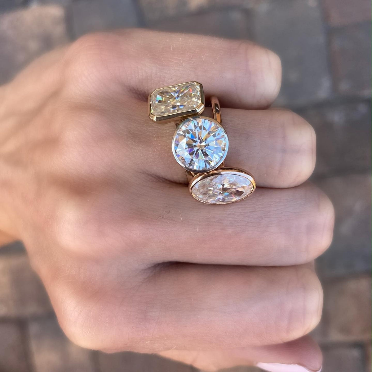 Close-up of a hand wearing stacked gold bezel engagement rings with round, oval, and geometric stones.
